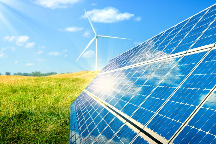 Solar Panels And Wind Turbines In Grassy Field With Sunlight