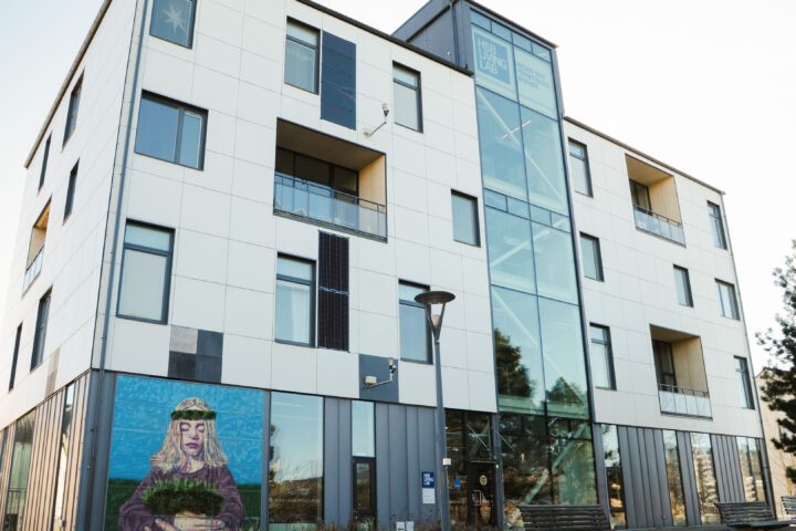 White building with large glass entrance and a mural of a woman holding a plant